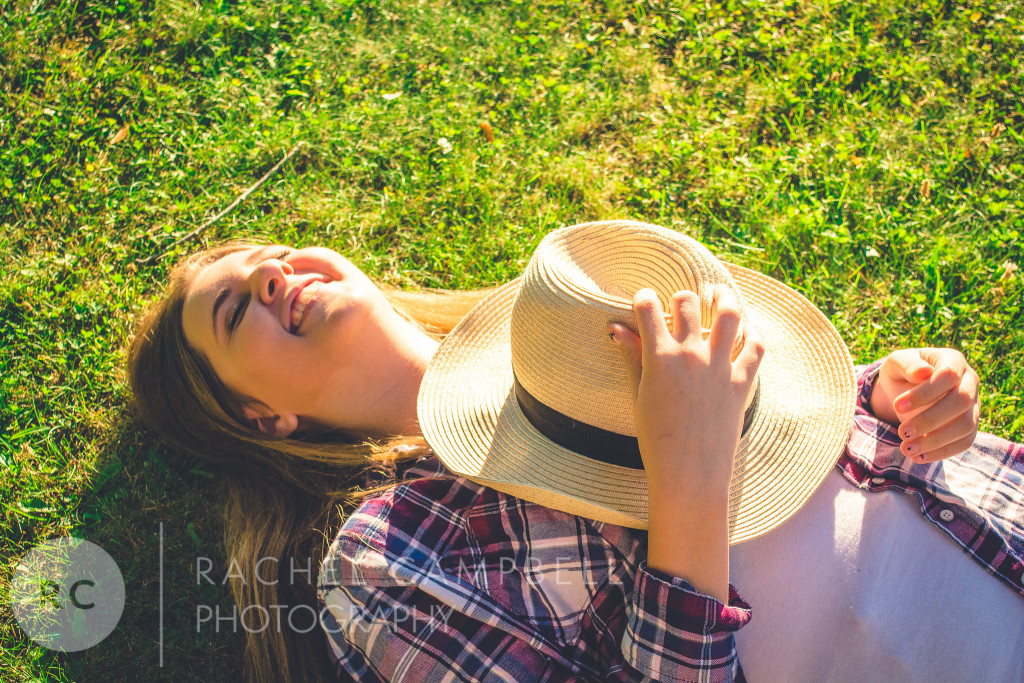 Senior portrait of a young woman laying in the grass holding a cowboy hat in Solon Ohio