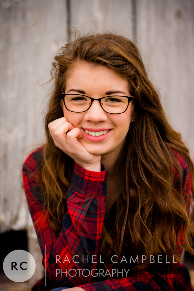 Senior portrait of a young woman wearing flannel sitting in front of a barn in Solon Ohio