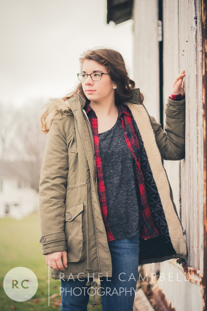 Senior photo of a young woman leaning against a barn wearing a winter coat in Solon Ohio