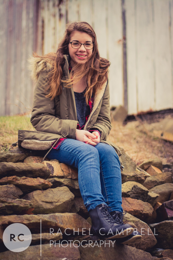 Senior portrait of a young woman leaning against a barn wearing a winter coat in Solon Ohio