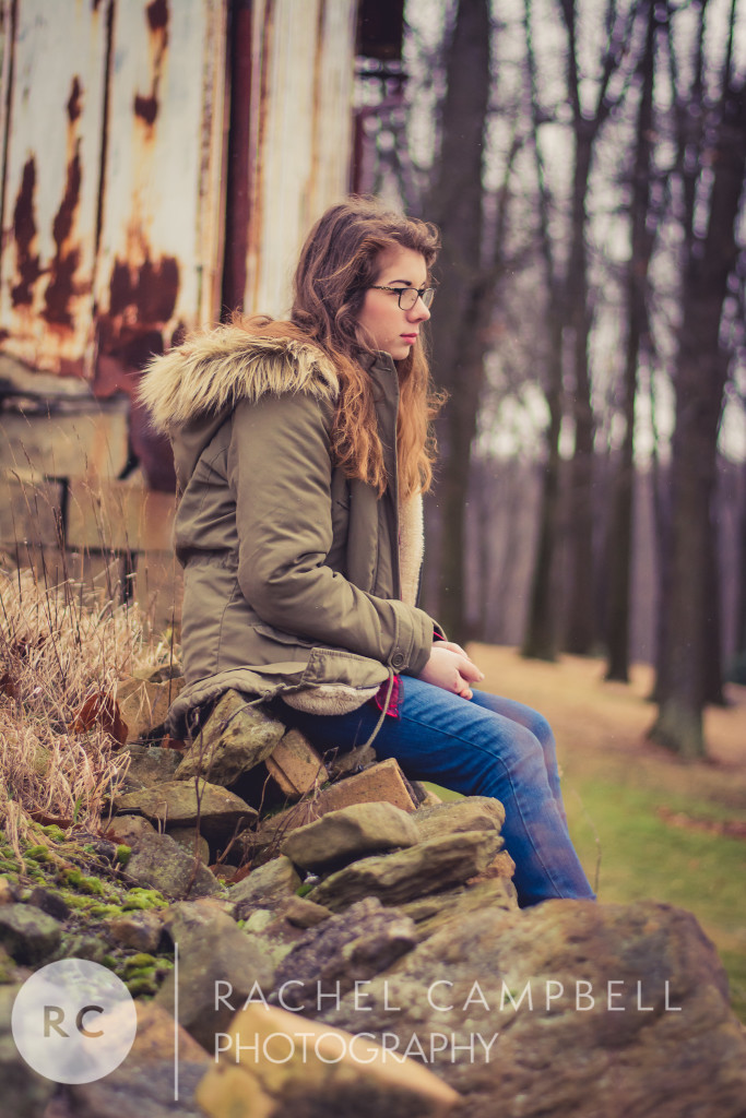Senior portrait of a young woman sitting on a rock wall wearing a winter coat in Solon Ohio