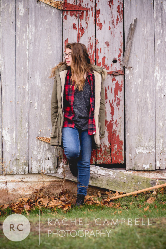 Senior portrait of a young woman wearing a winter coat standing in front of a barn in Solon Ohio