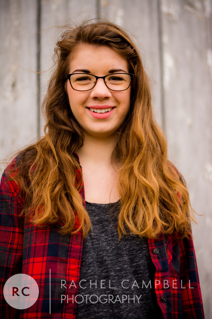 Senior portrait of a young woman wearing flannel standing in front of a barn in Solon Ohio