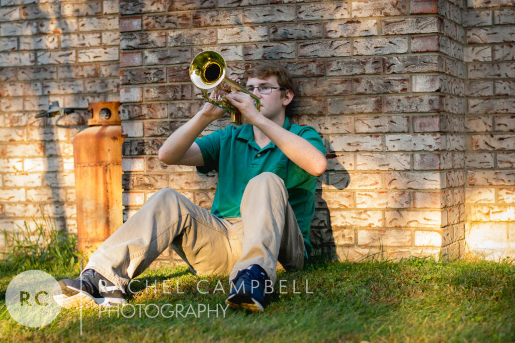 Senior picture of a young man leaning against a brick wall playing his trumpet in Solon Ohio