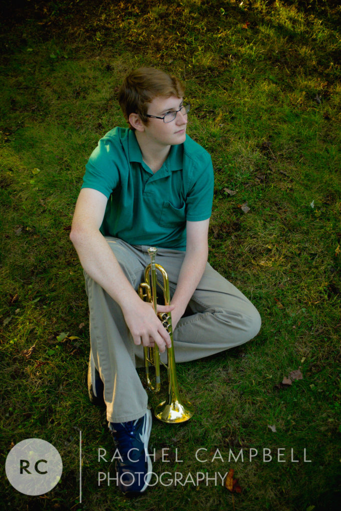 Senior portrait of a young man sitting in a patch of grass holding his trumpet in Solon Ohio