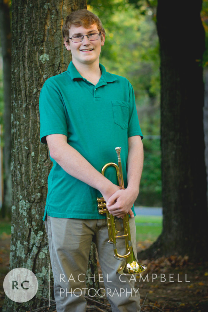 Senior protrait of a young man leaning against a tree with his trumpet in Solon Ohio