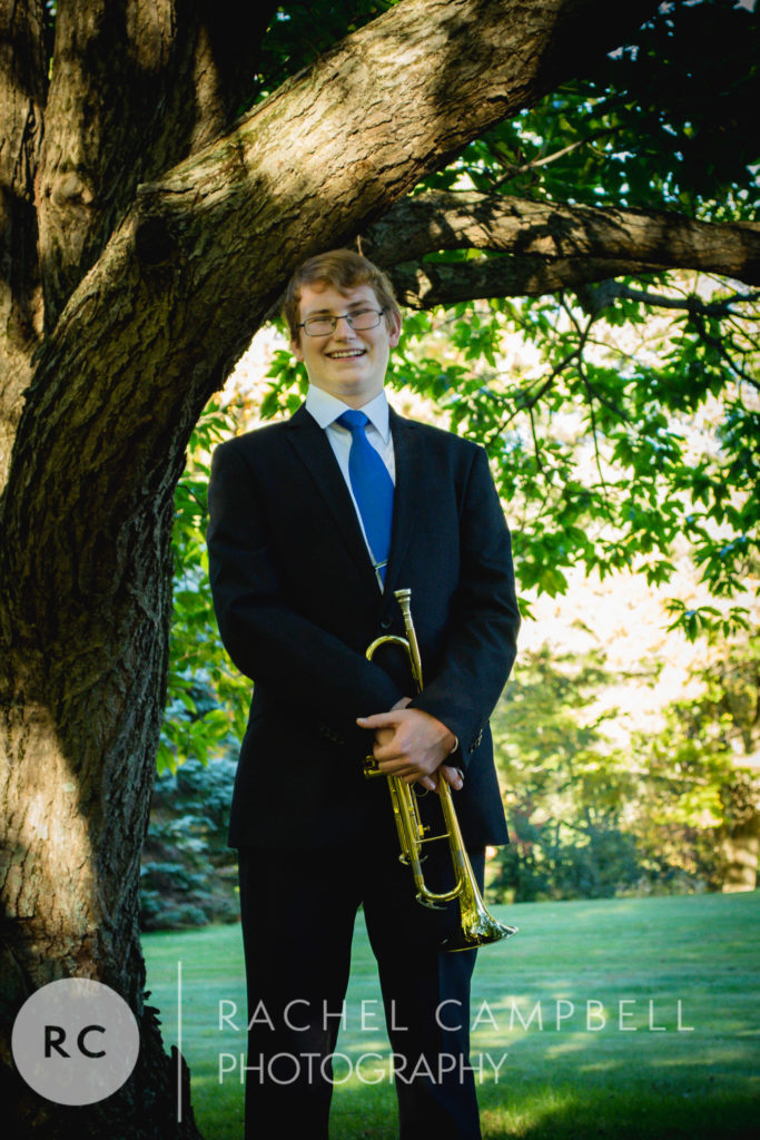 Senior portrait of a young man standing under a tree and holding his trumpet in Solon Ohio
