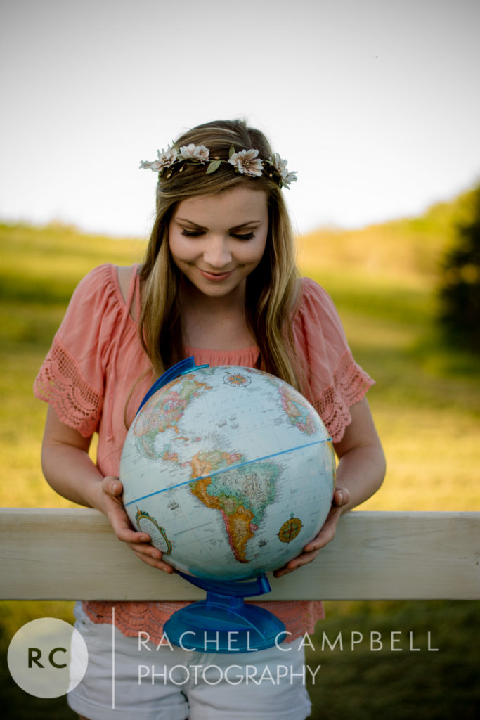 Senior photo of a young woman leaning over a fence holding a globe in Solon Ohio