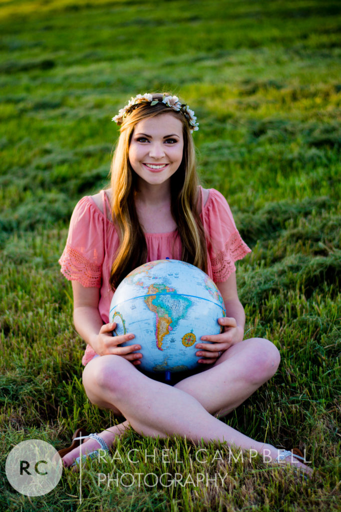 Senior portrait of a young woman sitting in a field while holding a globe at sunset in Solon Ohio