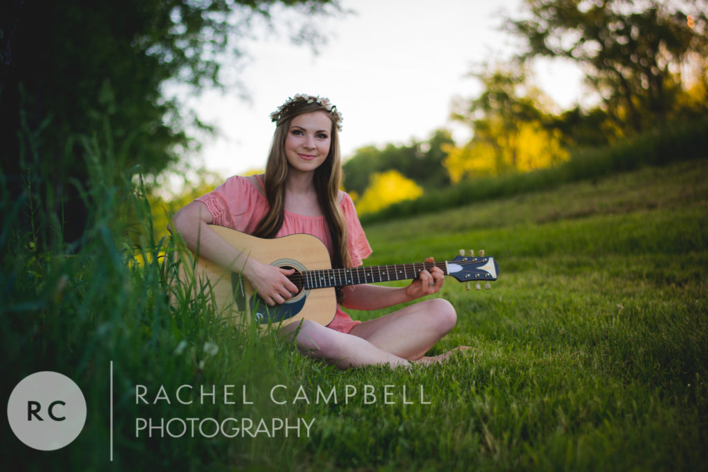 Senior portrait of a young woman sitting in a field at sunset playing guitar in Solon Ohio