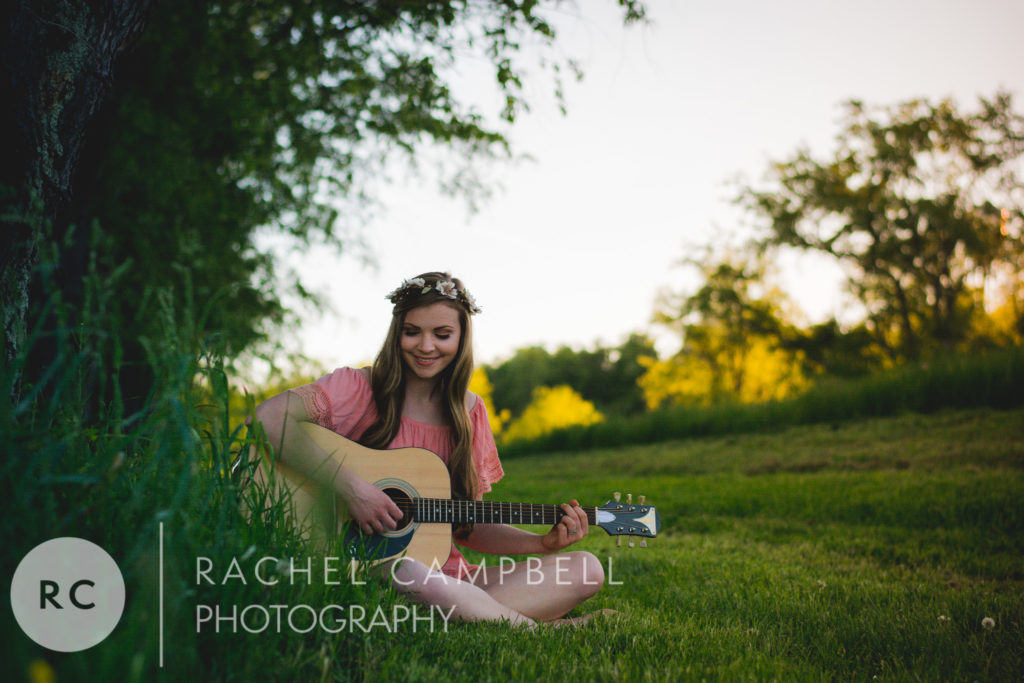 Senior portrait of a young woman playing guitar in a field at sunset in Solon Ohio
