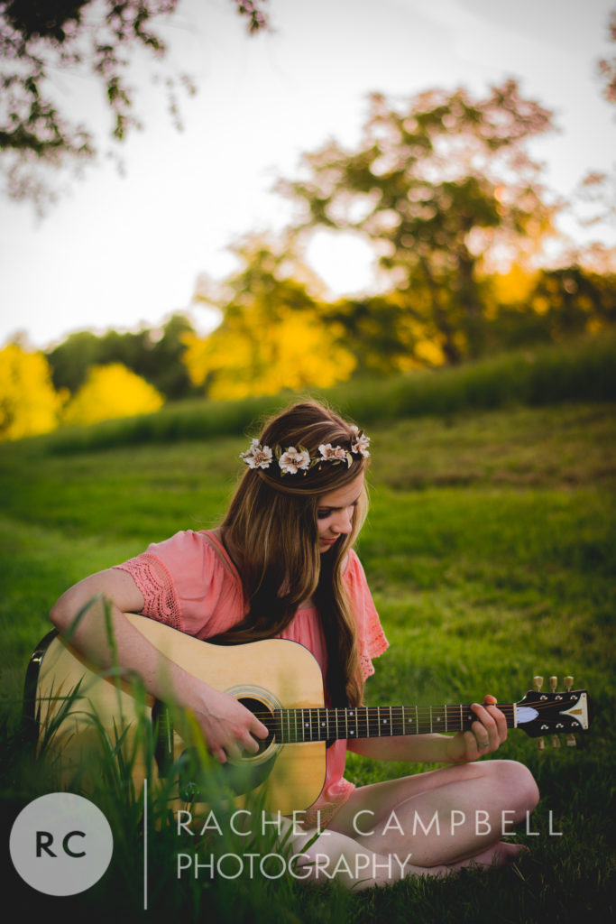 Senior portrait of a young woman playing guitar in a field at sunset in Solon Ohio