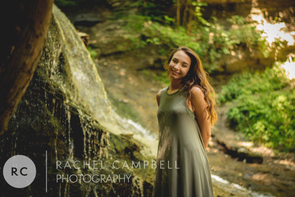 Senior photo of a young woman standing in front of a waterfall in the woods in Solon Ohio