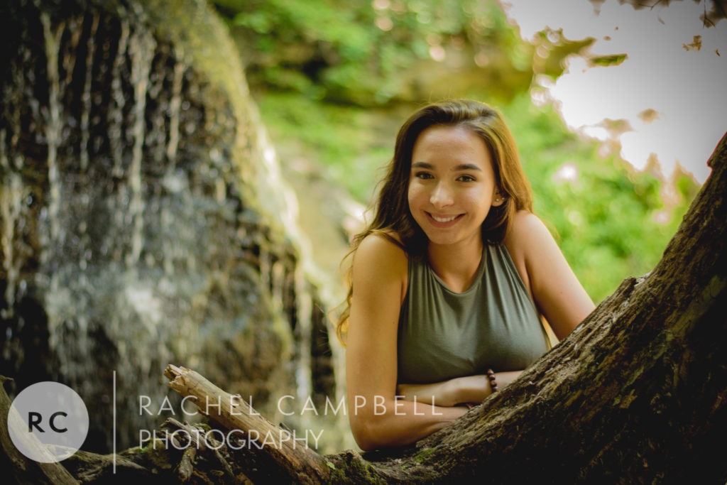 Senior picture of a woman leaning on a tree in front of a waterfall in the woods in Solon Ohio