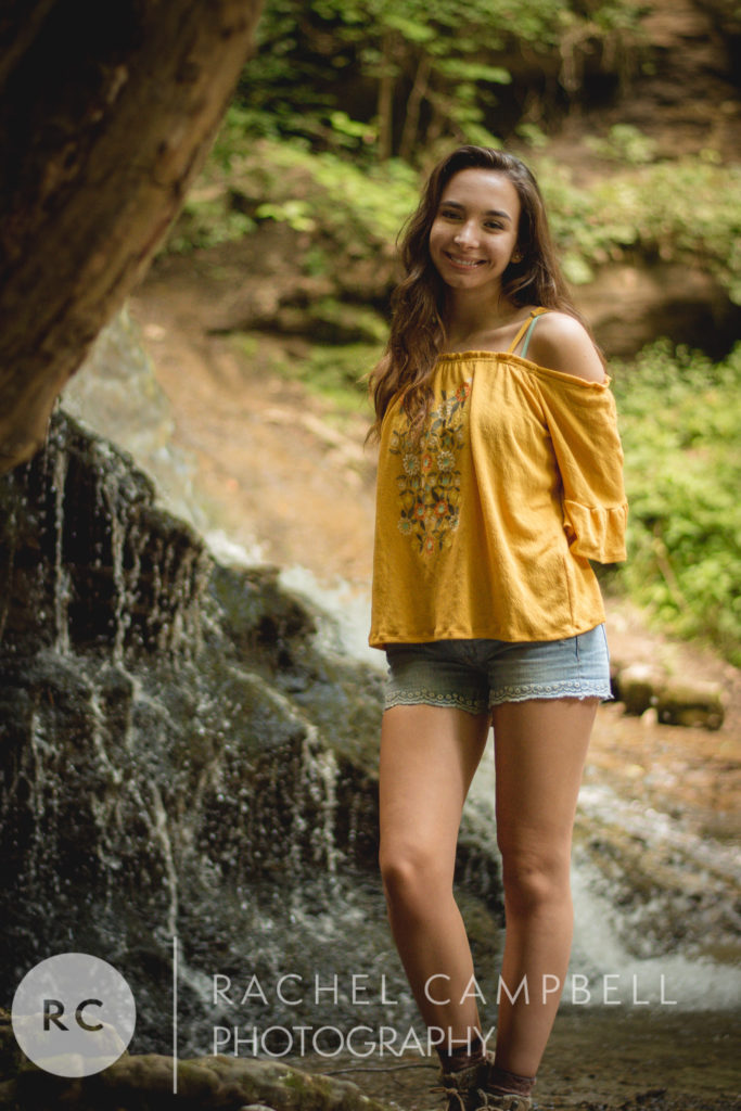 Senior portrait of a young woman standing in front of a waterfall in the woods in Solon Ohio