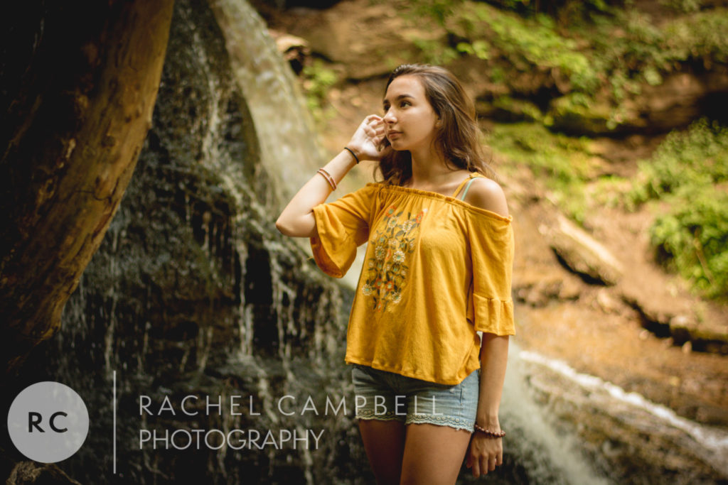 Senior portrait of a young woman standing near a waterfall in the woods in Solon Ohio