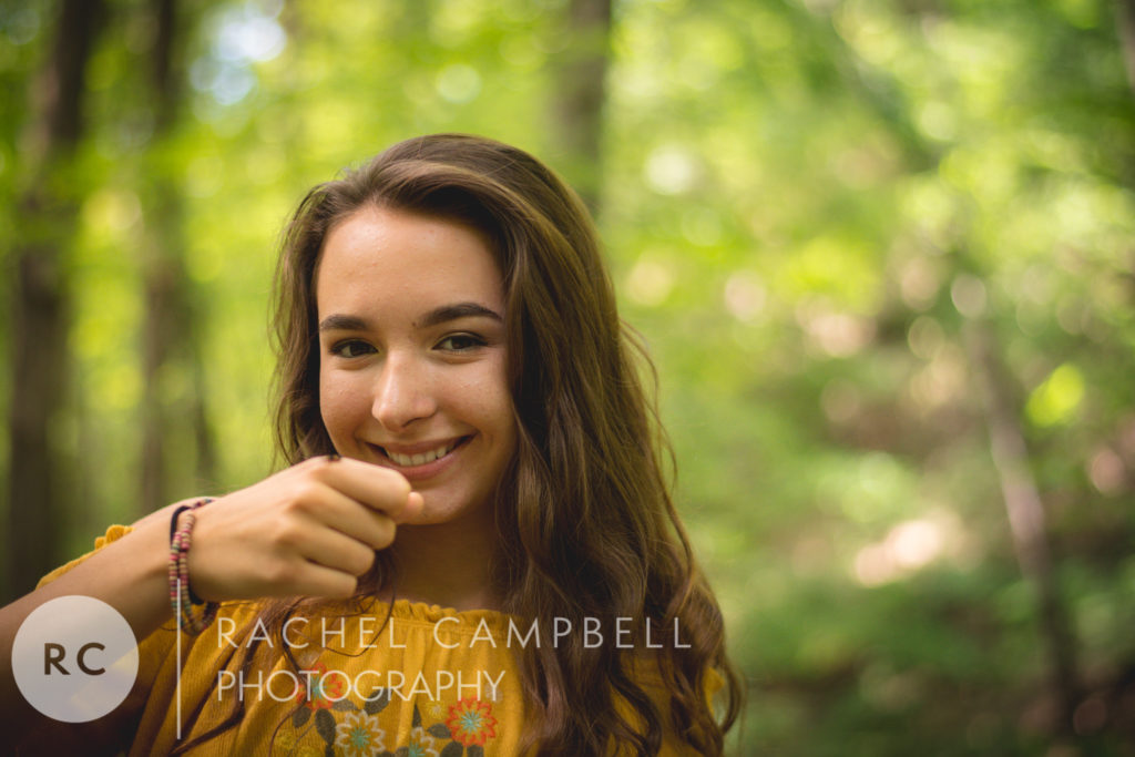 Senior portrait of a young woman smiling while a bug crawls on her hand in the woods in Solon Ohio