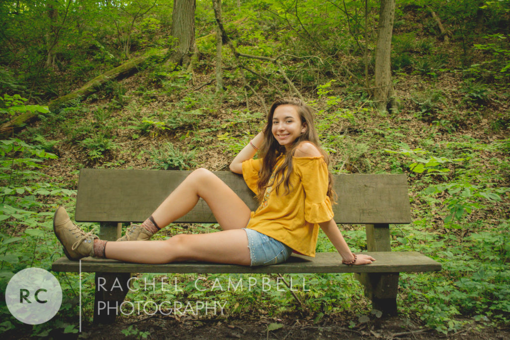 Senior photo of a young woman sitting on a bench in the woods in Solon Ohio.