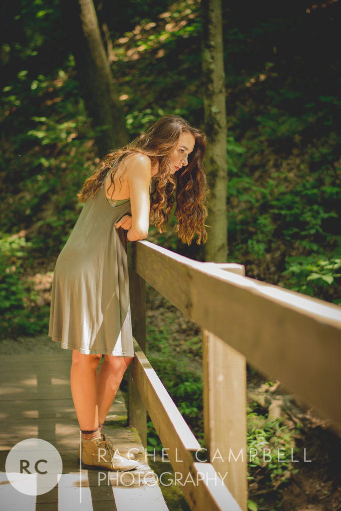 Senior portrait of a young woman looking down over a bridge in the woods in Solon Ohio