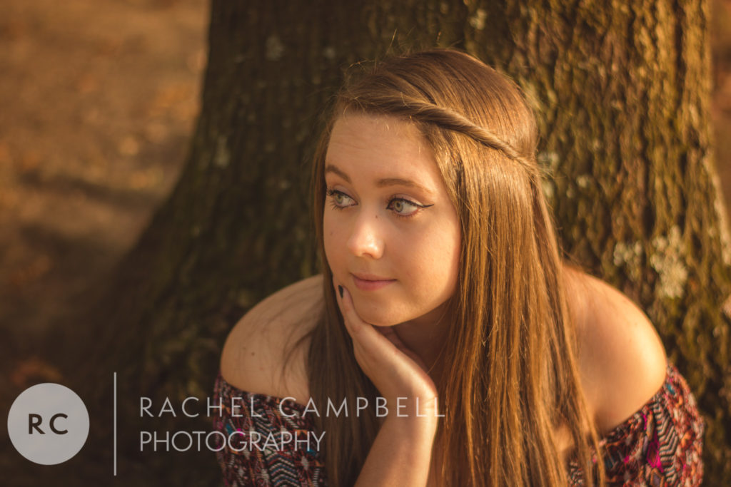 Senior portrait showing a young woman sitting against a tree at sunset in Solon Ohio