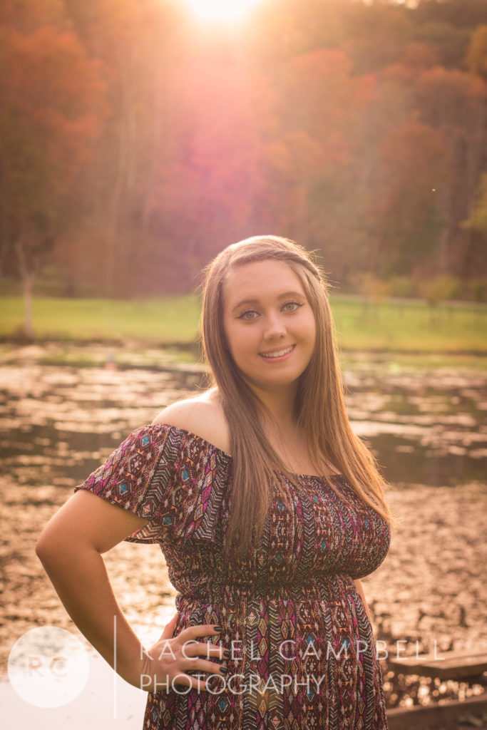 Senior photo showing a young woman near a pond at sunset