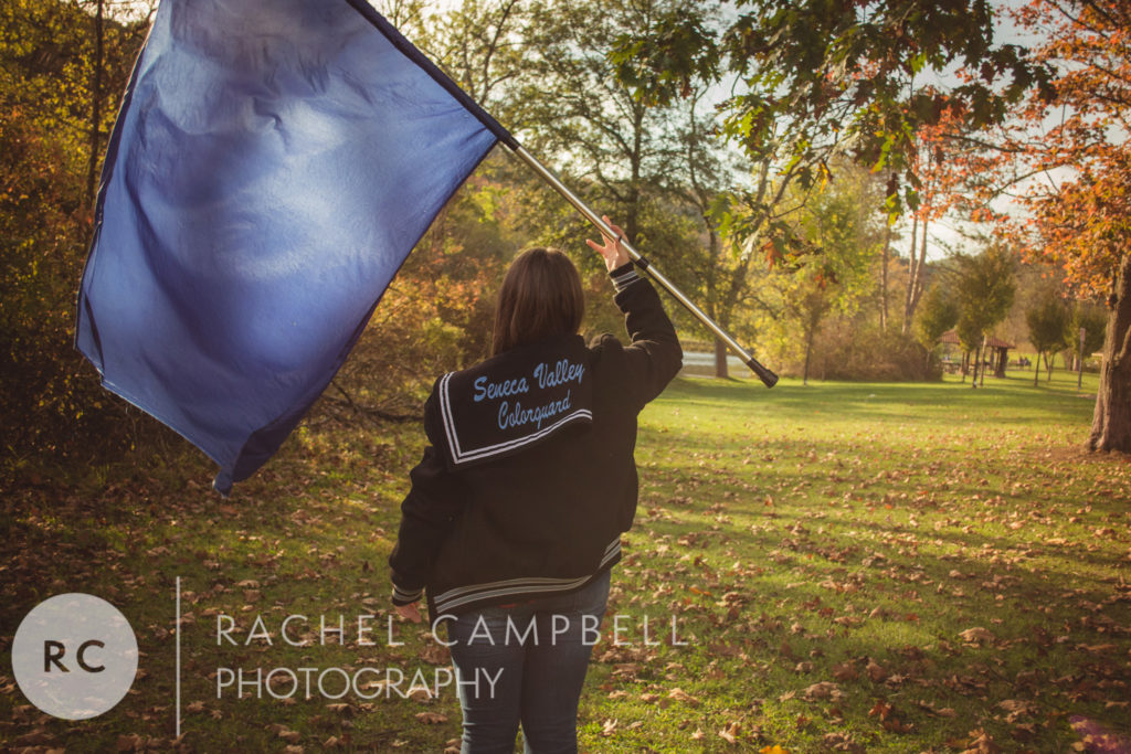 Senior portrait showing a young woman holding her color guard flag and wearing her varsity jacket in a park in Solon Ohio
